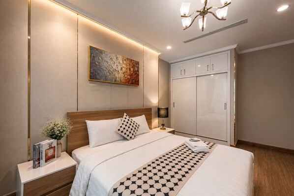 Quarto de hotel com uma cama grande, mesa de cabeceira, luminária, quadro na parede e um guarda-roupa.