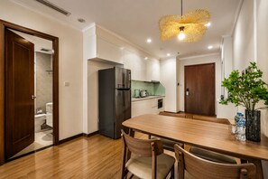 A compact kitchen with a refrigerator, a dining table with chairs, and a hanging light fixture. - Vinhomes Skyline Apartment Saigon (Ho Chi Minh City)