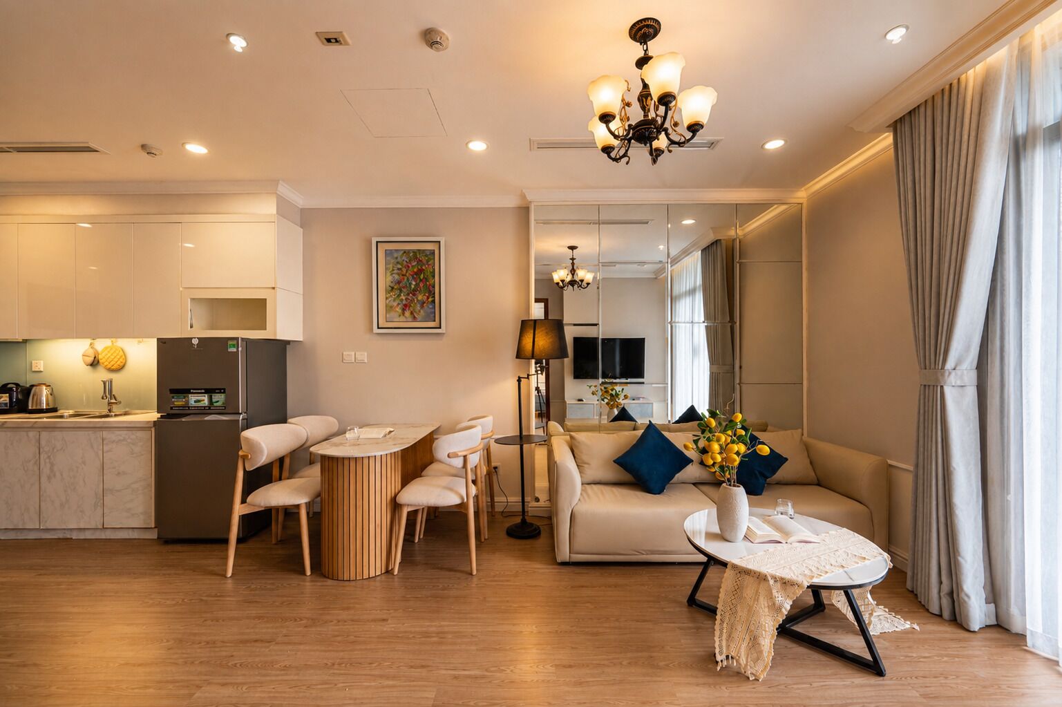 Un salon moderne comprenant un canapé, une table à manger et des chaises, un coin cuisine avec un réfrigérateur et une cuisinière, et une grande fenêtre avec des rideaux.