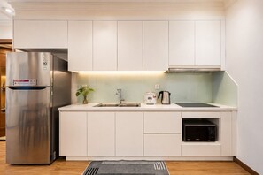 A modern kitchen with white cabinetry, a stainless steel refrigerator, a sink, a kettle, and an oven. - Vinhomes Skyline Apartment Saigon (Ho Chi Minh City)