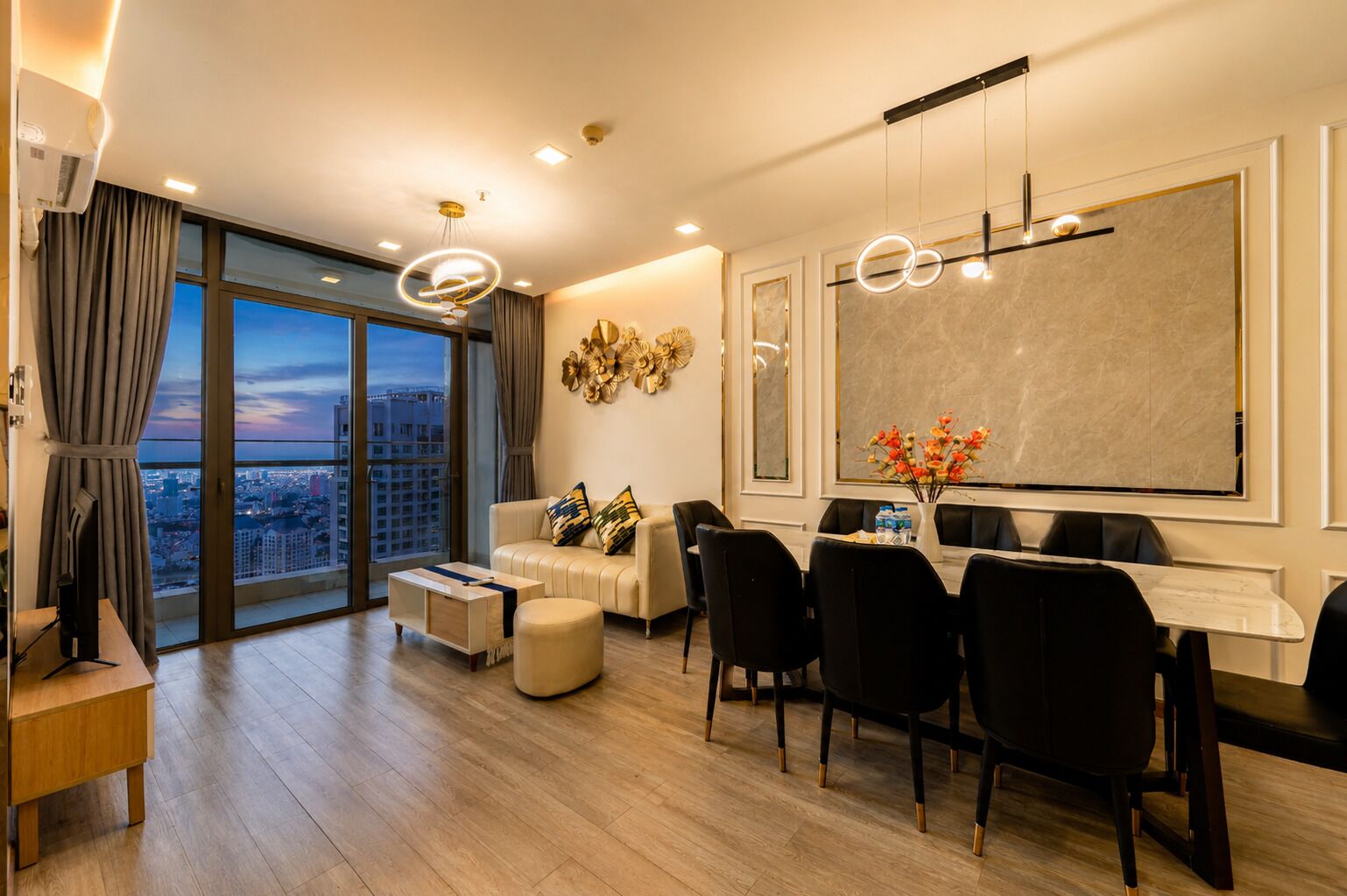 A modern living room with a sofa, dining table, chairs, and a large window with a city view.