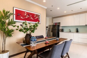 A dining area with a table, chairs, a vase with flowers, and a kitchen in the background. - Vinhomes Skyline Apartment Saigon (Ho Chi Minh City)
