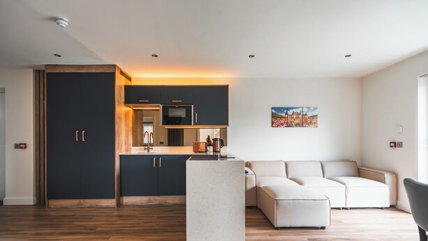 Una cocina moderna con armarios oscuros, una isla central y un área de comedor con un sofá y una silla.