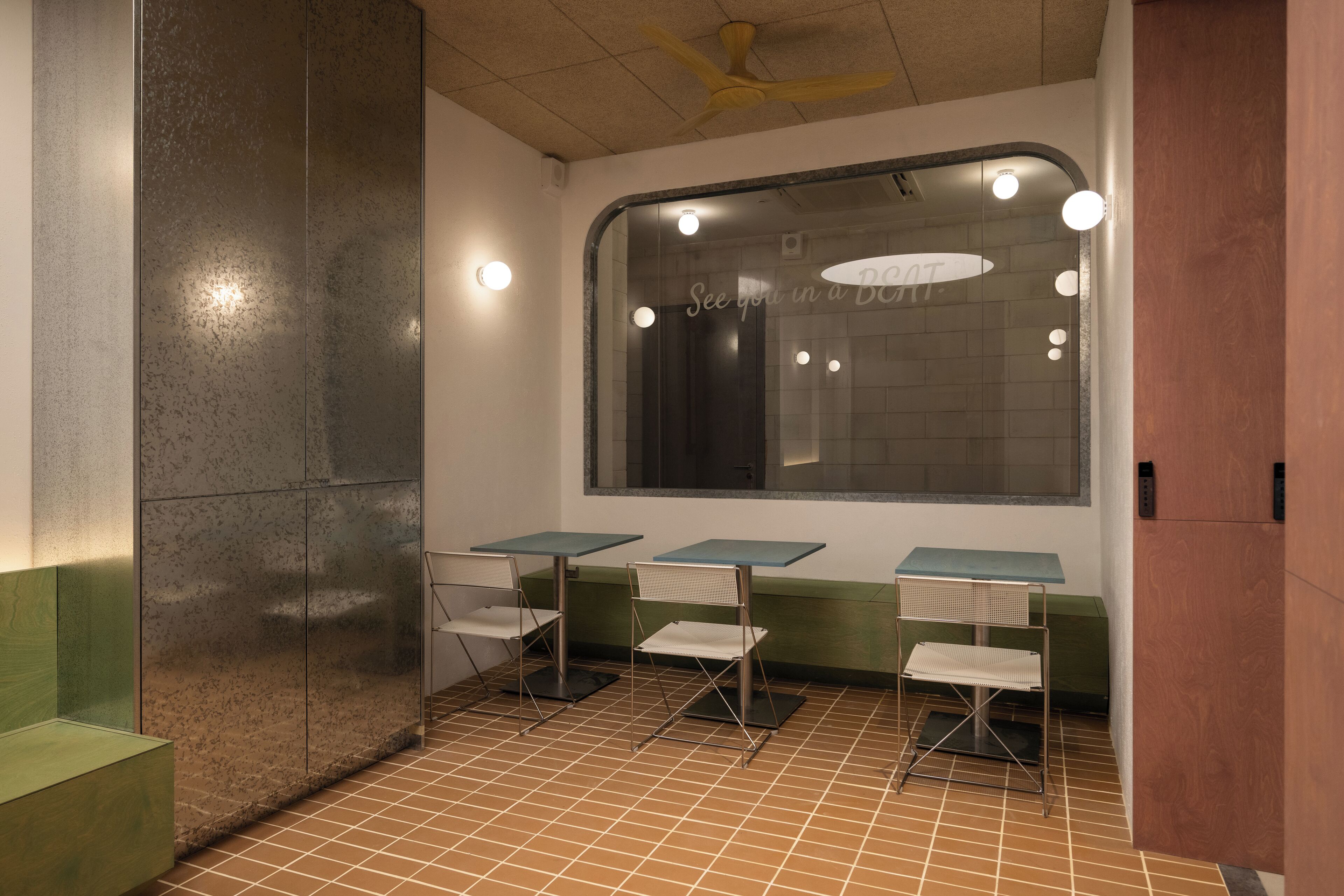 A waiting area with a large window, a ceiling fan, and a green bench.