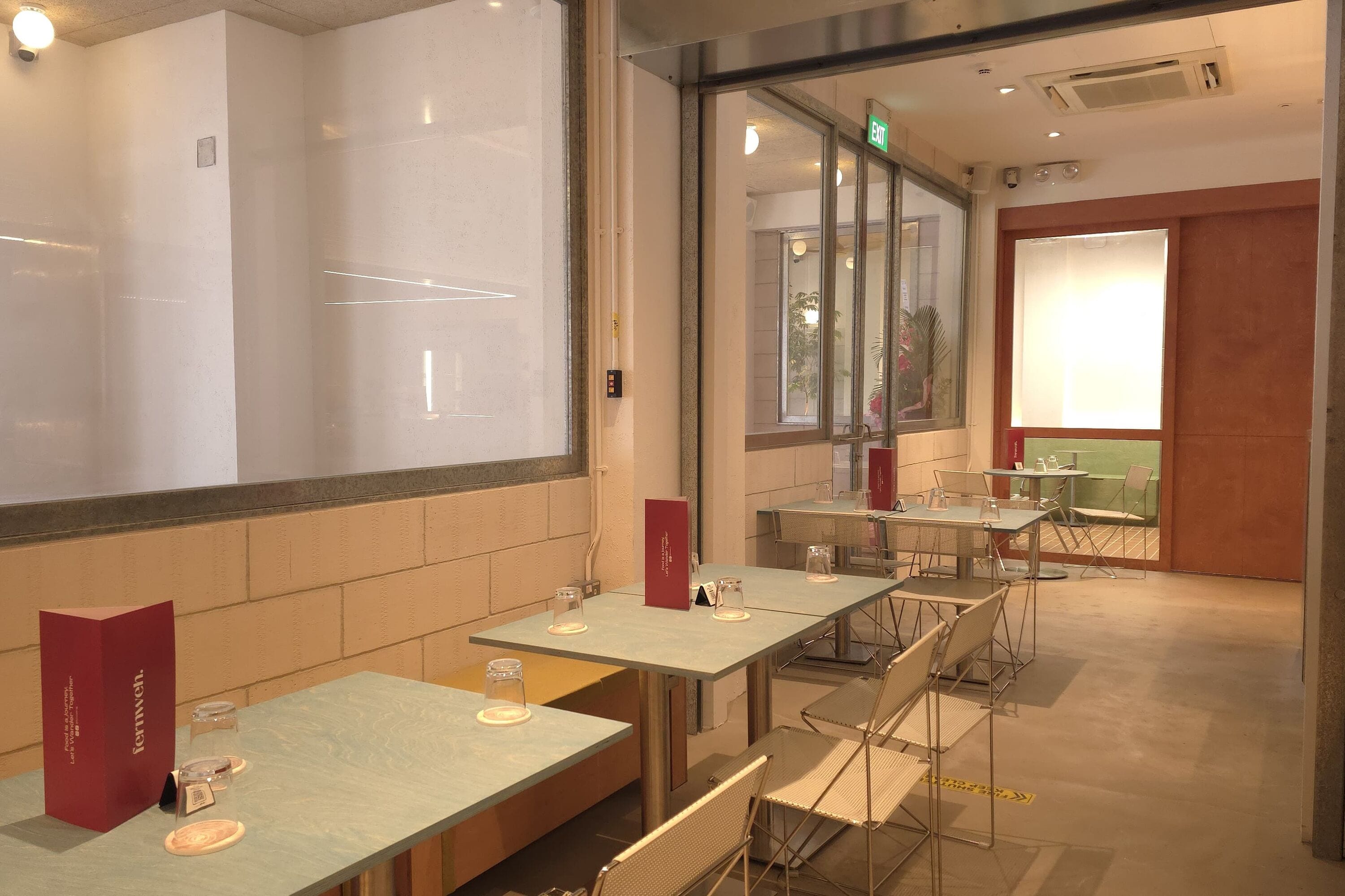 A restaurant with tables and chairs, a menu stand, and a glass partition.