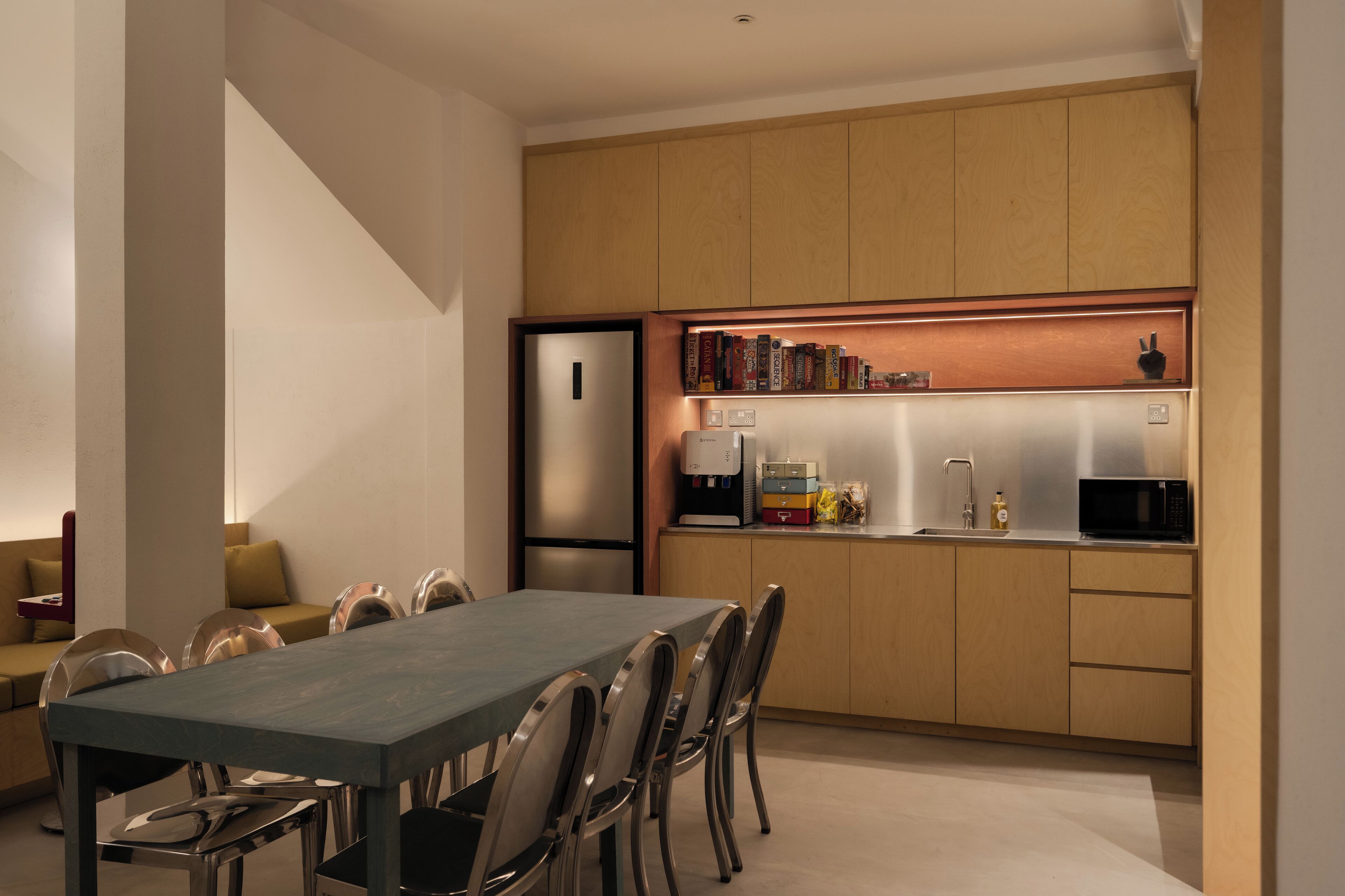 Una cocina moderna con comedor, que incluye una mesa larga, sillas, un refrigerador, un microondas y una cafetera.
