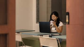 A person sitting at a table with a laptop, holding a cup, in a room with a mirror and a sign that says "See you".