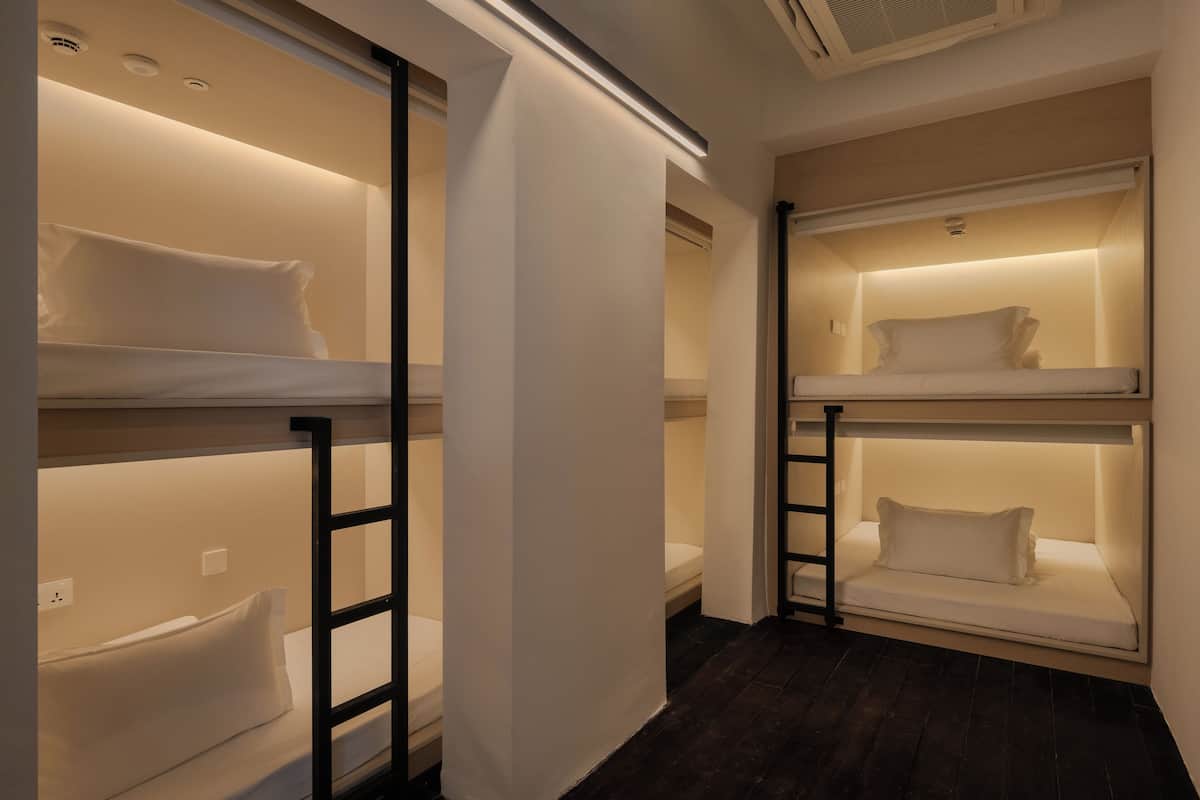 Habitación de hotel con literas, una escalera y una lámpara en el techo.