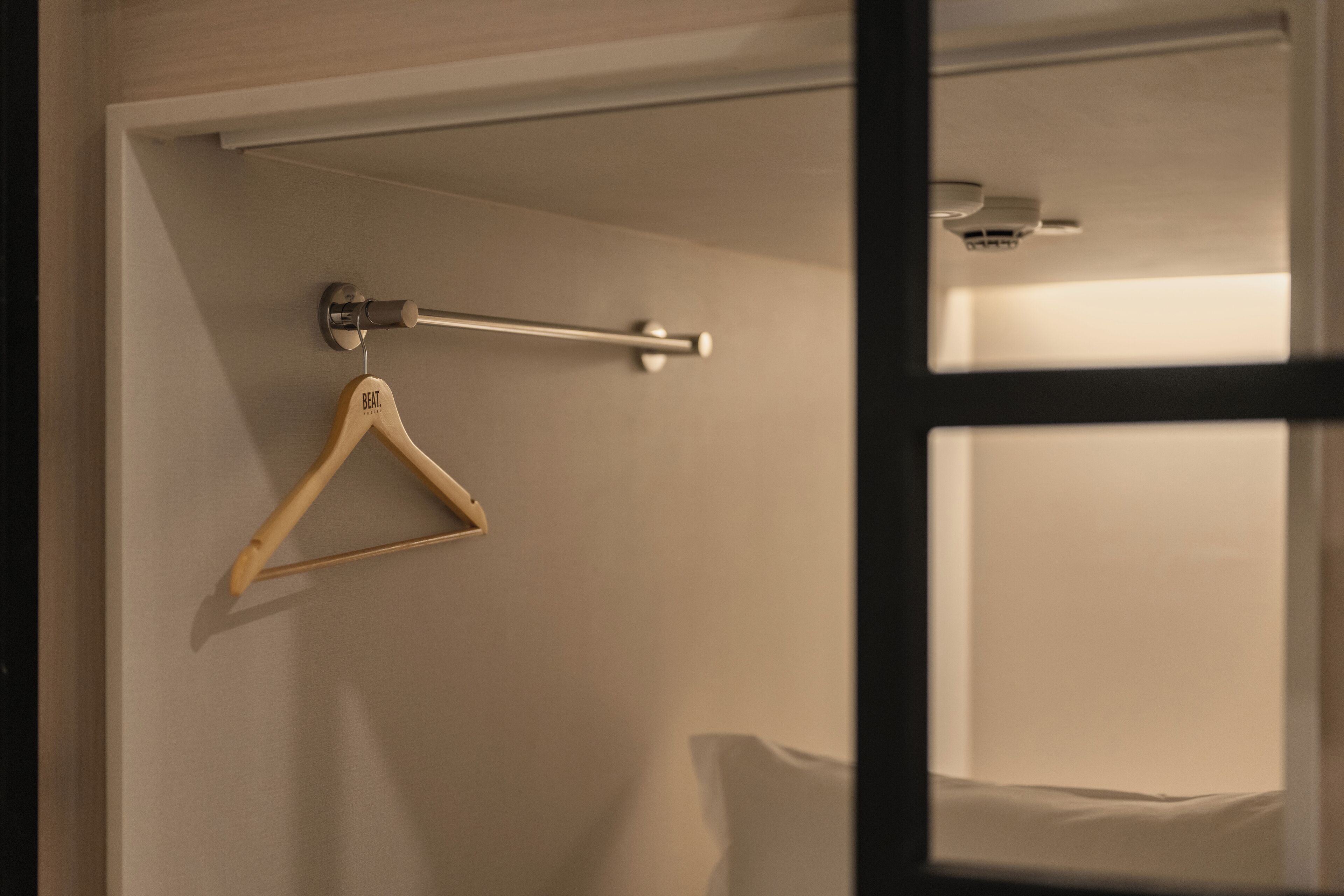 A room with a wooden hanger on the wall, a metal rod, and a ceiling-mounted light fixture.
