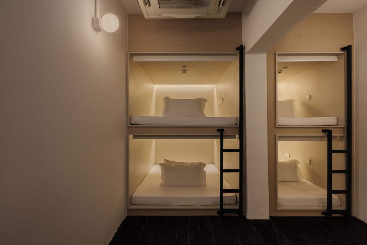 Habitación con literas, una escalera, un respiradero en el techo y una lámpara fijada a la pared.