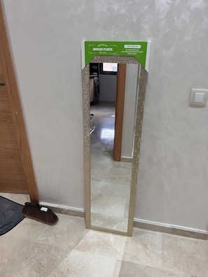 Un espejo con una etiqueta verde en la pared, un escoba y un piso de baldosas.