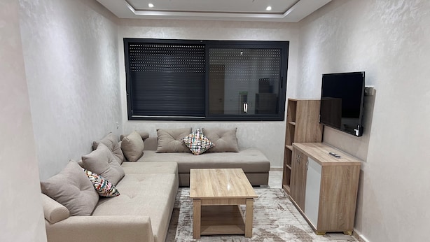 A modern living room with a beige sectional sofa, a wooden coffee table, and a TV on a wooden cabinet.