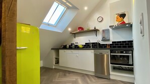 A kitchen with a skylight, a yellow refrigerator, white cabinets, a stainless steel dishwasher, and an oven. - Cosy loft in the heart of the Perche region (Val-au-Perche)