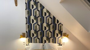 A bedroom with a geometric-patterned headboard, a bed with a yellow and brown bedspread, two bedside lamps, and a blue bench. - Cosy loft in the heart of the Perche region (Val-au-Perche)