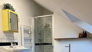 A modern bathroom with a glass shower, a sink with a mirror, and a wooden floor. - Cosy loft in the heart of the Perche region (Val-au-Perche)