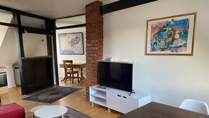 A living room with a TV, a red couch, a dining table, and a fireplace. - Stay in a Historic Half-Timbered House (Nürnberg)