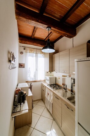 Eine kleine Küche mit Holzausstattung, einem Gaskochfeld, einem Kühlschrank und einem Fenster mit Vorhängen.
