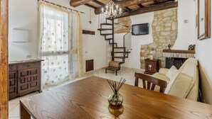 Un comedor con mesa de madera, sillas, candelabro y pared de piedra con un televisor.