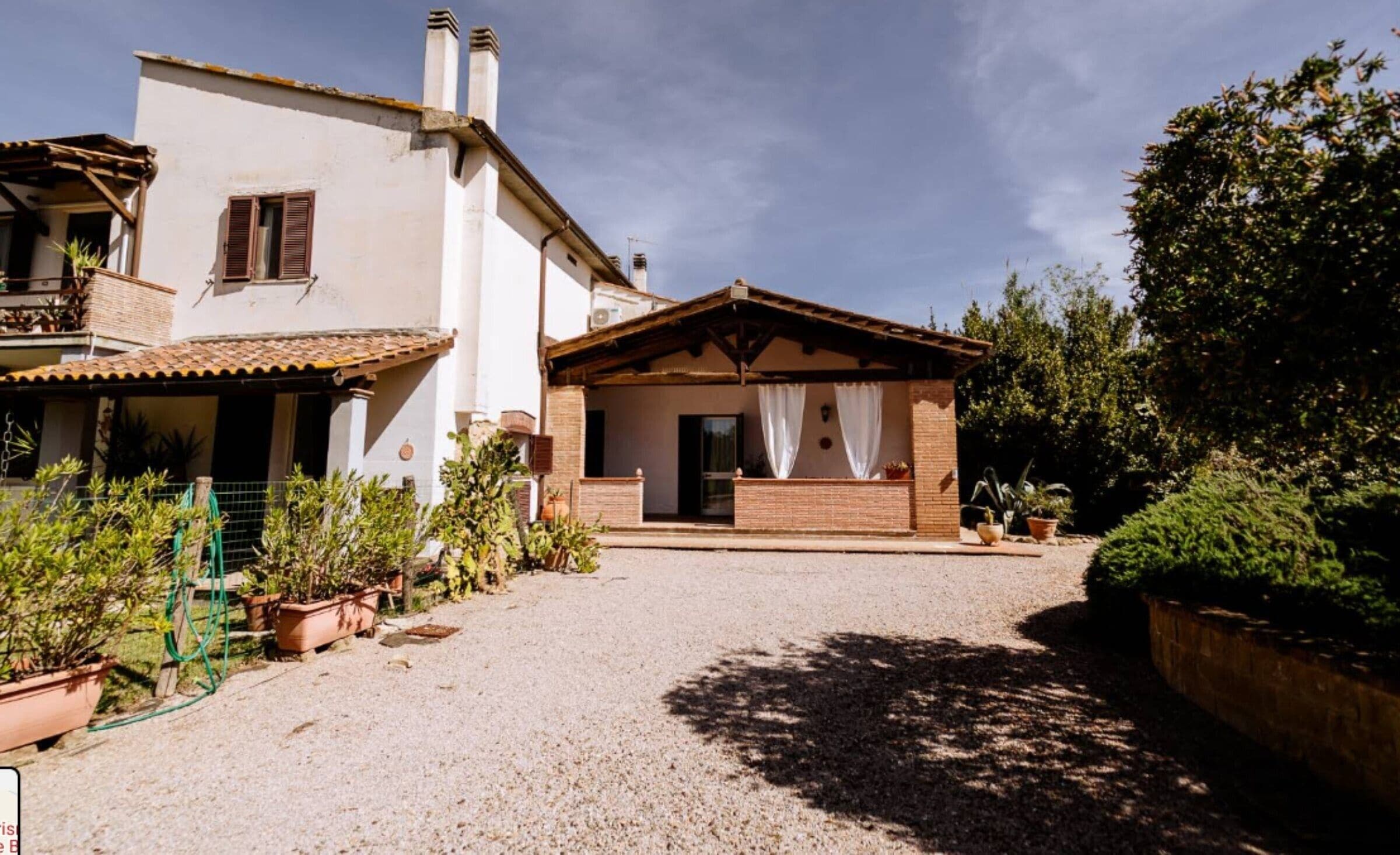 Una casa a due piani con un portico coperto, vialetto in ghiaia e piante in vaso.