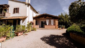 Una casa de dos pisos con un porche cubierto, camino de entrada de grava y plantas en macetas.