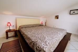 Een keurig opgemaakt slaapkamer met een bed, bedlampen, een klein tafeltje, een bankje, een vloerkleed en een wandplank met een plant.