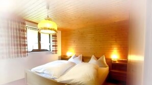 Une chambre avec un plafond en bois, un lit avec une literie blanche, deux lampes de chevet et une fenêtre avec des stores.