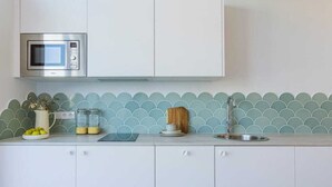 A kitchen with white cabinets, a stainless steel microwave, a sink, and a backsplash with a scalloped pattern.
