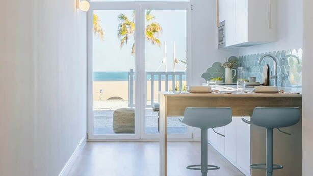 A modern hotel room with a large sliding glass door leading to a balcony with a beach view.