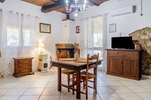 Un coin repas comprenant une table en bois, des chaises, une cheminée, un téléviseur et un mur en pierre.