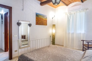 Une chambre à coucher avec un lit, un miroir, un tableau, une fenêtre avec des rideaux et une chaise.