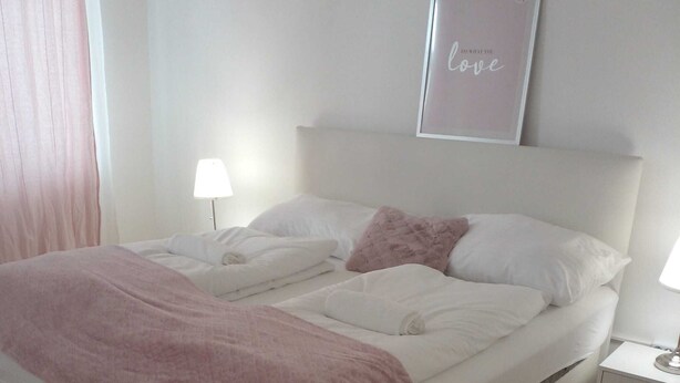 Ein ordentlich gemachtes Bett mit rosa Bettdecke und Kissen, einer Nachttischlampe und einem gerahmten Schild an der Wand.