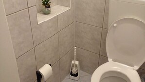 Ein Badezimmer mit Toilette, Papierhalter, Bürste und einer kleinen Pflanze auf einem Regal.