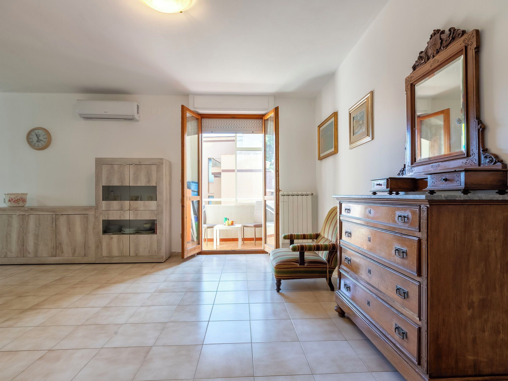 Ein geräumiges Zimmer mit einem Holzkabinett, einem großen Spiegel und einem Sessel.