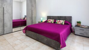A bedroom with a large bed, a nightstand, a lamp, and a mirror.