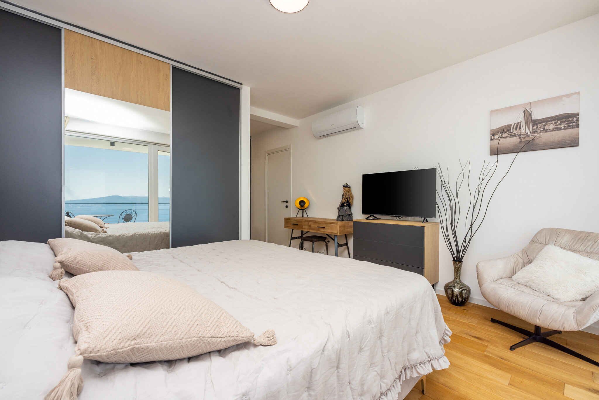 A bedroom with a bed, a desk, a chair, a TV, and a window with a view.