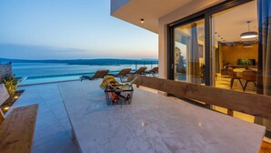 Zona relax esterna moderna con vista sul mare, un banco di legno e un tavolo con un cesto di oggetti.