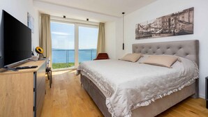 Una camera da letto con un letto grande, una TV, una scrivania e vista mare attraverso un'ampia finestra.