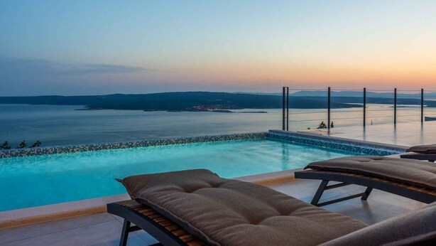Una piscina a sfioro con vista sul mare e sulla terraferma al tramonto.