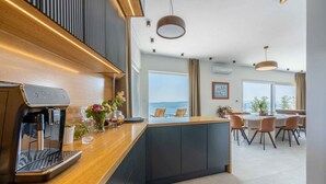 Una cucina moderna con una macchina per espresso integrata, un piano di lavoro in legno e vista sull'area pranzo, con sedie e un tavolo.