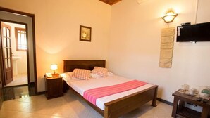 A bedroom with a wooden bed, a nightstand with a lamp, a wall-mounted TV, and a small table with a kettle. - Kings Court Residency  (Ampiyiya)