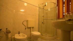 A bathroom with a toilet, bidet, sink, and a glass-enclosed shower. - Kings Court Residency  (Ampiyiya)