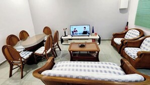 Ein Wohnzimmer mit Esstisch, Stühlen, einer Couch, einem Couchtisch und einem Fernseher.