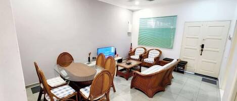 A dining area with a round table and chairs, a sofa, a ceiling fan, and a wall-mounted TV.