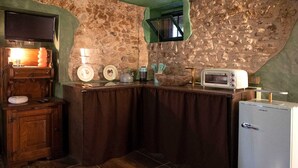 Uma cozinha com parede de pedra, armário de madeira, geladeira branca e bancada com diversos utensílios.