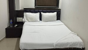 A neatly made bed with white linens, a dark headboard, and a window above. - Hotel Ajwa (Mumbai)