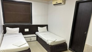 A small, clean room with two single beds, a dark headboard, a small cabinet, and a door. - Hotel Ajwa (Mumbai)