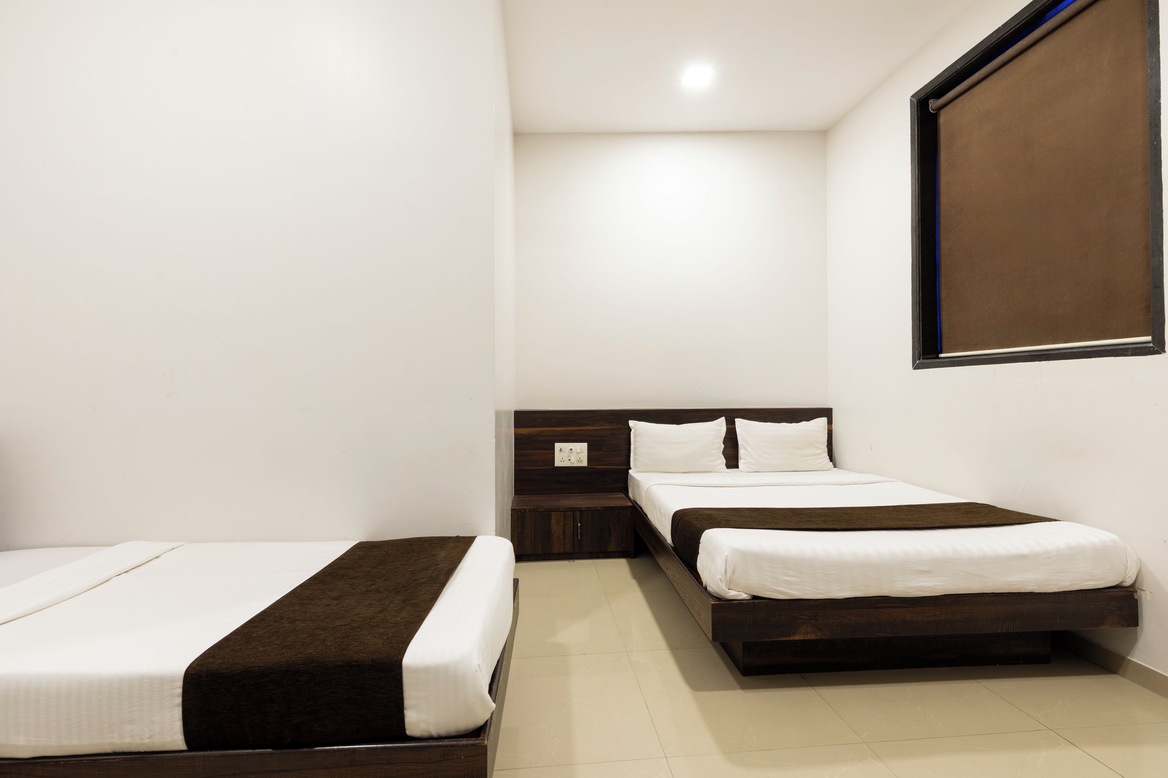 A hotel room with two single beds, a wooden headboard, a small bedside table, and a wall-mounted TV.