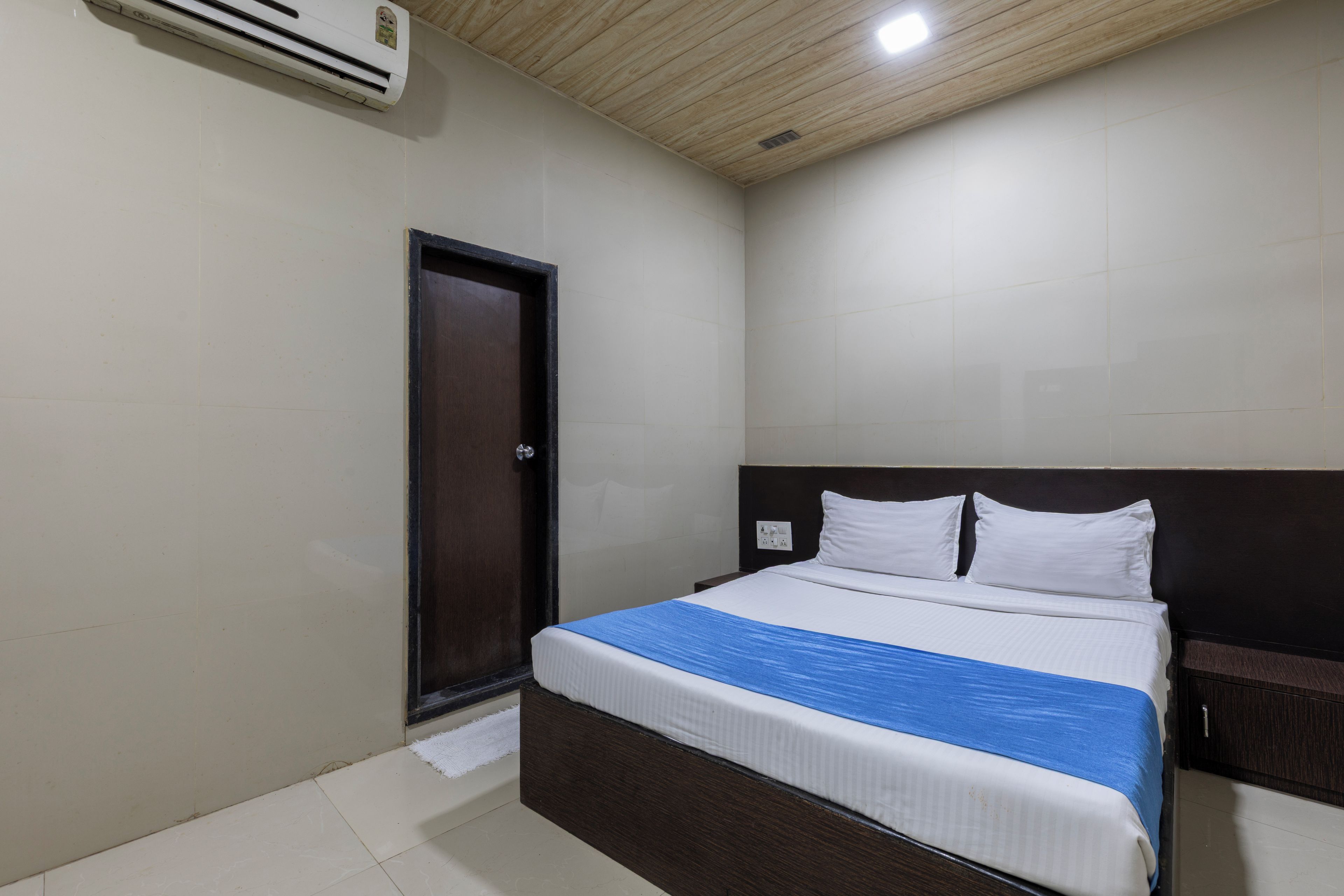A hotel room with a bed, a door, and a ceiling vent.