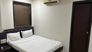 A single bed with a headboard, a bedside table, a wall-mounted air conditioner, and a door. - Hotel Ajwa (Mumbai)