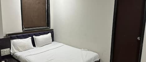A single bed with a headboard, a bedside table, a wall-mounted air conditioner, and a door.
